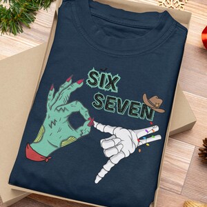 May include: Navy blue t-shirt with the text "SIX SEVEN" and graphic hands. One hand is green with red nails, the other is a white skeleton hand with colorful lights. A cowboy hat graphic is also included.