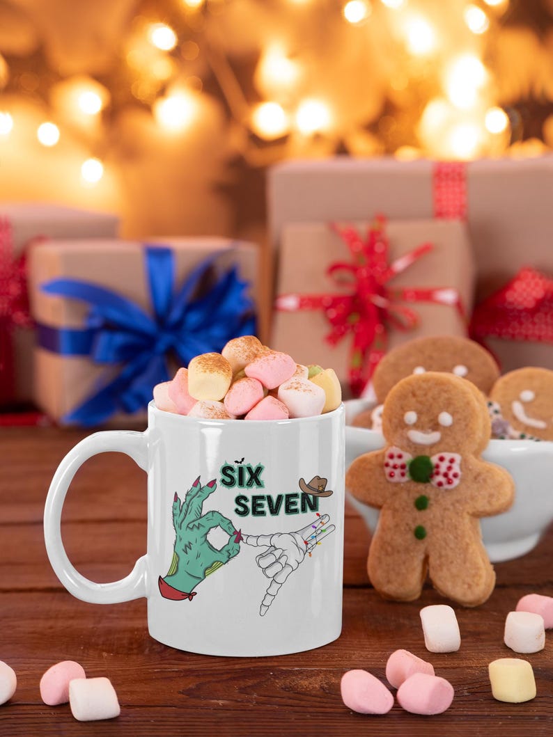 May include: White ceramic mug filled with marshmallows, featuring a graphic of two hands, one green and one skeletal, with the text "Six Seven". A gingerbread man and wrapped gifts are in the background.