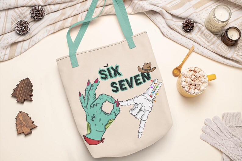 May include: Beige tote bag with teal handles featuring a Halloween-themed design. The design includes the text "SIX SEVEN", a cowboy hat, and two hands, one green and zombie-like, the other a skeleton hand.