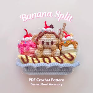 Puede incluir: Un postre de banana split tejido a ganchillo con una figura de oso, helado y una cereza. El texto "Banana Split" está arriba y "PDF Crochet Pattern Dessert Bowl Accessory" abajo.