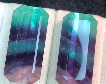 May include: Two rectangular fluorite crystals with a gradient of colors. The crystals transition from a light pink at the base to purple, then teal, and finally a vibrant green at the top. The facets catch the light.