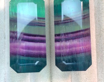May include: Two rectangular, faceted gemstones with a vibrant colour gradient. The stones transition from a deep teal at the edges to a purple and lavender centre, with a hint of blue. The gems are likely for jewellery making.