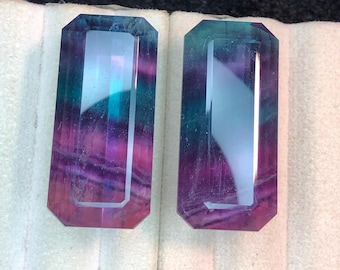 May include: Two rectangular, faceted gemstones with a mix of purple, teal, and clear colors. The stones have a polished appearance and are set against a light background. The gemstones are likely for jewelry making.