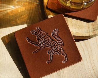 May include: Brown leather coaster with a detailed wolf design. The coaster is on a wooden surface.