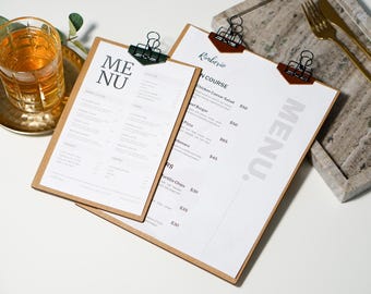 May include: Two brown clipboards with white paper menus. The top menu has the word "MENU" in large, bold, white letters. The bottom menu has a list of food items and prices. The menus are on a white surface.
