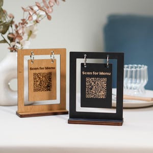 May include: Two wooden table signs, one light brown and one black, each with a QR code and the text "Scan for Menu." The signs are rectangular with a cutout frame and a small base. They are displayed on a white surface.