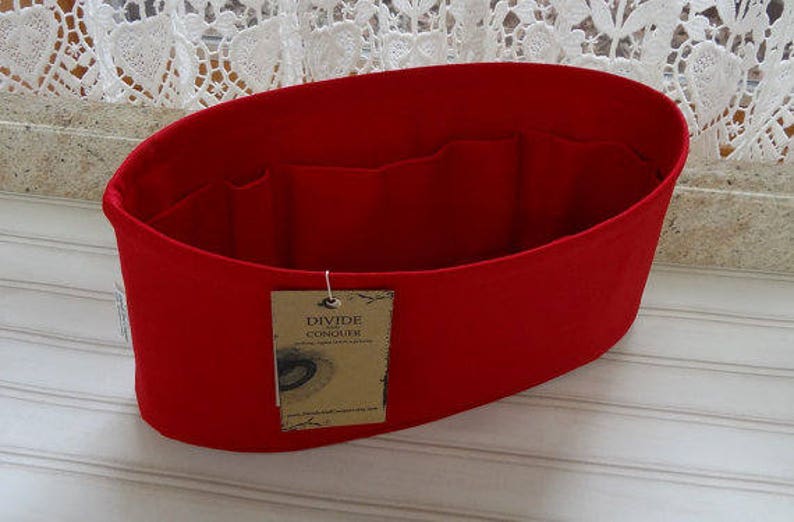 May include: A bright red felt bag organizer with multiple interior pockets. The organizer has a tag that reads "DIVIDE CONQUER". The bag is designed to help organize the contents of a larger bag or tote.