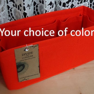 May include: Bright orange felt bag organizer with multiple compartments. The text "Your choice of color" is displayed on the front. A tag with the words "DIVIDE AND CONQUER" is attached to the side.