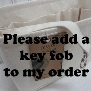 May include: A white canvas tote bag with multiple compartments. The bag has a black strap and a silver key fob attached. The text "Please add a key fob to my order" is printed on the bag.