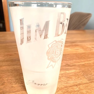 Könnte beinhalten: Ein gefrostetes Glas mit den Worten "Jim Beam" und einem Logo mit dem Text "Jim Beam Since 1795" darauf gedruckt. Das Glas hat das Wort "Jamie" auf dem Boden geschrieben.