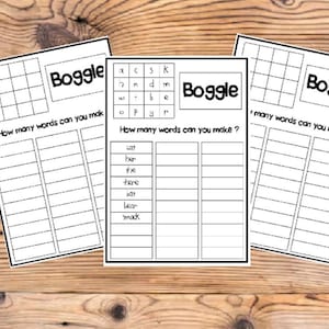 Op de afbeelding: Drie Boggle-spelbladen op een houten oppervlak. Elk blad heeft een raster om woorden in te schrijven en het woord "Boggle" bovenaan. De tekst "How many words can you make?" is ook zichtbaar.
