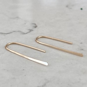 May include: A pair of gold-toned minimalist earrings with a simple, curved design. The earrings are made of thin metal and have a slightly hammered finish.
