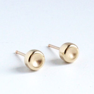 May include: A pair of gold stud earrings with a rounded, slightly concave design. The earrings are simple and elegant.
