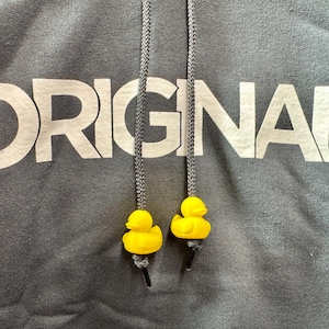 May include: A grey hoodie with the word "ORIGINAL" printed in white on the front. The hoodie has two black drawstrings with yellow rubber ducky charms.