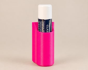 May include: A bright hot pink plastic holder containing a cylindrical lip balm tube with a white cap and a dark blue label featuring the text CLASSIC. The holder has a smooth, curved exterior and is designed to securely store the balm.