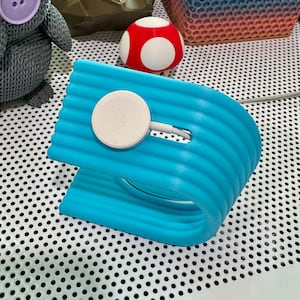 May include: A blue, wavy, charging stand for a smartwatch. The stand has a white, round charging pad.