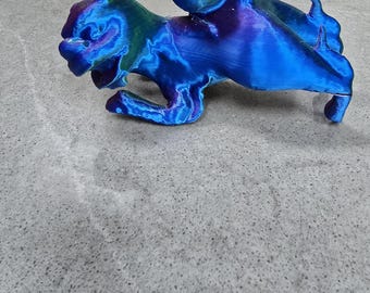 Puede incluir: Una figurita de una criatura mítica con alas, impresa en 3D, de color azul, verde y morado. La criatura está de pie sobre sus patas traseras con las alas extendidas.