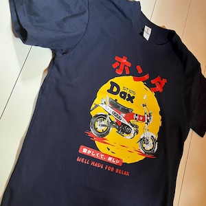 Może przedstawiać: Granatowa koszulka z żółtym okręgiem z grafiką czerwono-białego motocykla. Koszulka zawiera japoński tekst i angielskie wyrażenie "Well Made For Relax".