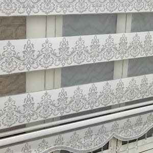 Könnte beinhalten: Weißer Rollo mit silbernem Glitzermuster und einer Perlenborte. Der Rollo ist hochgezogen, so dass der weiße Stoff darunter sichtbar ist.