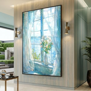 May include: Large framed painting showing a window with white curtains and a sea view. A vase of white and peach flowers sits on the windowsill. The artwork is mainly blue and white, creating a serene atmosphere.