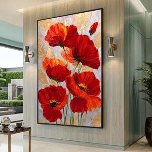May include: A framed painting of red poppies with black centres and green stems. The background features gold leaf accents on a light grey and white textured surface. The artwork is displayed in a modern interior setting.