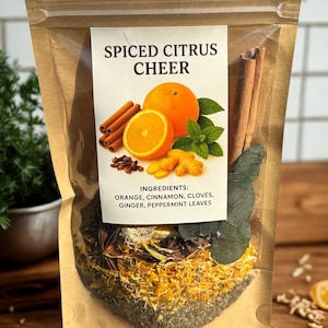 May include: A clear, resealable bag filled with ingredients for spiced citrus cheer. The bag features a label with the text "SPICED CITRUS CHEER" and illustrations of oranges, cinnamon sticks, and mint leaves. Ingredients listed include orange, cinnamon, cloves, ginger, and peppermint leaves.
