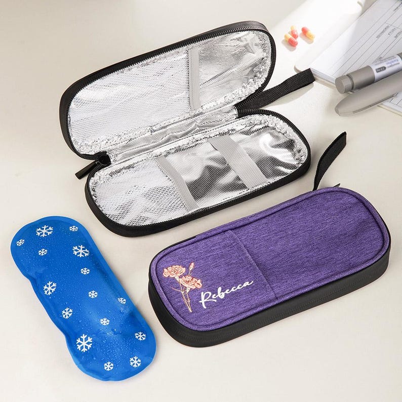 May include: An open black insulated case with a silver interior, a purple case with a floral design and the name "Rebecca", and a blue ice pack with white snowflakes. The cases have black zippers and handles.