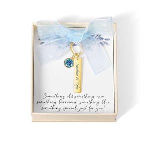 May include: A gift box with a light blue ribbon and a gold-colored charm. The charm has a blue gemstone and a rectangular tag with the names "Jonathan & Sofia". The box contains the text "Something old something new..."