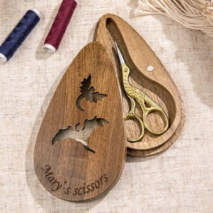May include: A wooden sewing kit with a bat design and the text "Mary's scissors." The kit contains gold-coloured scissors with a bird design. Two spools of thread are visible in the background.