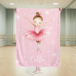 May include: A pink blanket with a watercolour illustration of a ballerina in a pink tutu and ballet shoes, arms outstretched. The blanket has a pattern of white stars and the name "Callie" in cursive.