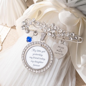 Può includere: Una spilla d'argento con un design floreale e cristalli trasparenti. La spilla ha una chiusura a spilla da balia e include un ciondolo rotondo con il testo "My little girl yesterday, my friend today, my daughter forever."