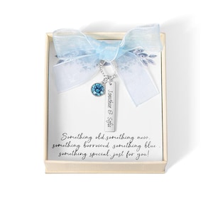 May include: A necklace with a blue gemstone and a rectangular pendant engraved with "Jonathan & Sofia" is displayed in a gift box. The box is decorated with a light blue ribbon. The text on the card reads "Something old something new..."