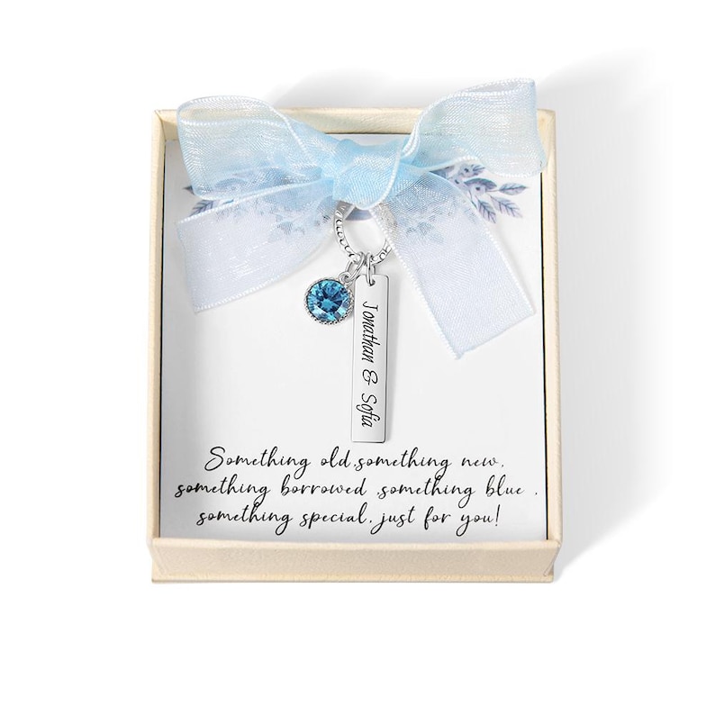 May include: A necklace with a blue gemstone and a rectangular pendant engraved with "Jonathan & Sofia" is displayed in a gift box. The box is decorated with a light blue ribbon. The text on the card reads "Something old something new..."