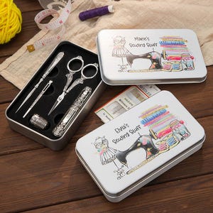 May include: A sewing kit with silver tools, including scissors, needles, and a thimble, is displayed in an open metal case. Two white metal boxes with illustrations of sewing machines and spools of thread are also visible.
