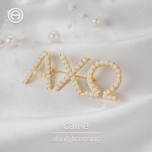 May include: Gold-toned brooch spelling out "AXΩ" with faux pearls. The letters are outlined in gold and filled with small, round, white pearls. The brooch is on a white satin background, with a string of pearls in the background.