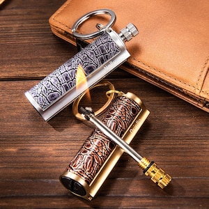 May include: Two refillable keychain lighters with a textured, crocodile-like pattern. One is silver with a gray and black design, the other is gold with a brown and gold design. The silver lighter has a flame lit. Both have a name engraved.