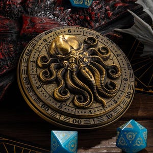 May include: A bronze-colored, round decorative piece with an octopus design in the center. The octopus has detailed tentacles and is surrounded by a circular border with numbers. The word "Benjamin" is inscribed on the octopus. Two blue dice are in the foreground.