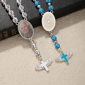 May include: Two rosaries with oval pendants. One features a portrait, the other a sunburst design. One has white beads with cross accents and a white cross pendant with wings. The other has blue beads and a blue cross pendant with wings.