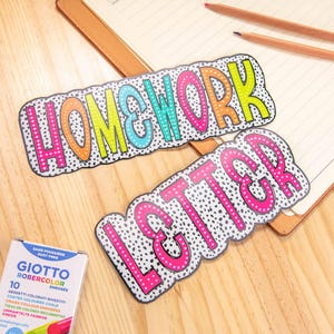 Puede incluir: Dos letreros de papel recortados con las palabras "HOMEWORK" y "LETTER" en letras en negrita y contorneadas. Las letras est&aacute;n rellenas de colores brillantes y rodeadas de un patr&oacute;n de lunares en blanco y negro. Se ve una caja de tiza Giotto Robercolor.