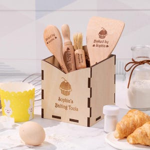 May include: A set of wooden baking tools, including a spoon, rolling pin, brush, and spatula, stored in a laser-cut wooden box. The box is engraved with a cupcake design and the text "Sophia's Baking Tools." Additional baking items are also present.