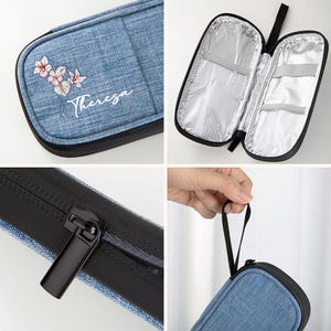 May include: A blue denim-style insulated lunch bag with a black zipper and handle. The bag features a floral design and the name "Theresa" printed on the front. The interior is silver and has mesh and elastic compartments.