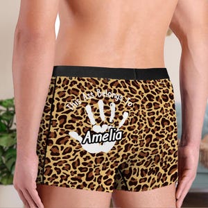 Puede incluir: Bóxers con estampado de leopardo. Los bóxers presentan el texto "This Ass Belongs to Amelia" con una huella de mano blanca. La cintura es negra.