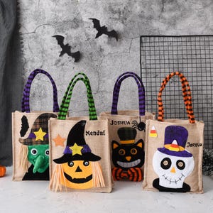 以下が含まれることがあります： カラフルなハンドルとアップリケのデザインが施された、4つのジュートハロウィーンのトリートバッグ。バッグには魔女、ジャック・オー・ランタン、黒猫、スカルが描かれています。各バッグには名前が書かれており、ハンドルはストライプです。