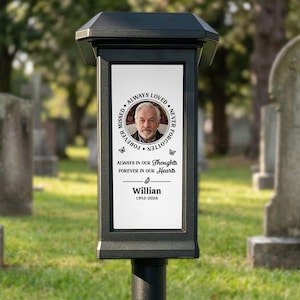May include: A black solar memorial light featuring a white rectangular panel with a circular portrait of a man, the text "ALWAYS LOVED NEVER FORGOTTEN FOREVER MISSED", "ALWAYS IN OUR THOUGHTS FOREVER IN OUR HEARTS", "Willian", and "1952-2026".