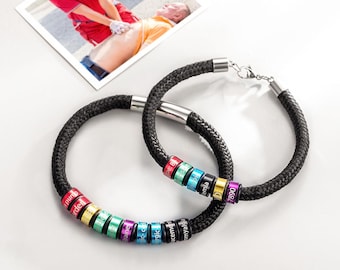 May include: Two black rope bracelets with colorful, engraved rings. The rings are in various colors, including red, green, blue, and purple. The bracelets have silver-colored clasps. A photo of a medical emergency is in the background.