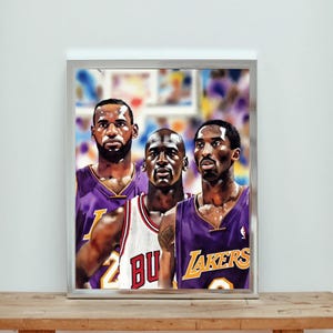 May include: Framed artwork featuring portraits of three basketball legends: LeBron James, Michael Jordan, and Kobe Bryant. The players are depicted in their team jerseys, with the Lakers and Bulls logos visible. The artwork is displayed in a silver frame.