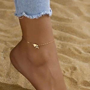 May include: Gold ankle bracelet with a heart charm and a letter 'A' charm.