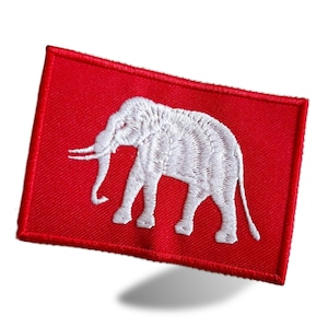 Op de afbeelding: Een rode stoffen patch met een wit geborduurd olifant. De olifant kijkt naar links en heeft zijn slurf omhoog.