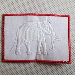 May include: White embroidered patch with a red border, featuring a white elephant silhouette.
