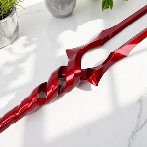 May include: A red, twisted, metal sculpture with a sharp point. The sculpture is made of two pieces of metal that are twisted together.
